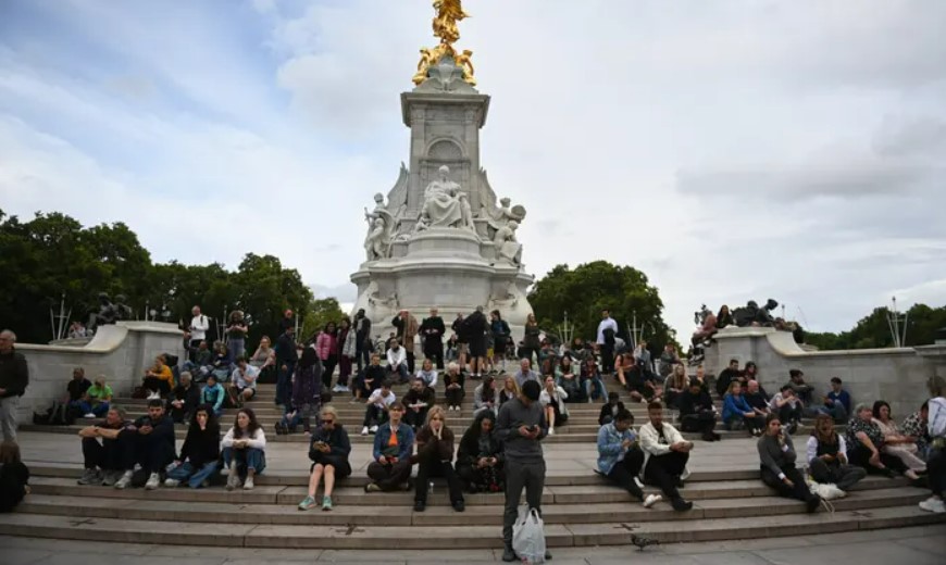 Люди сидят на ступенях мемориала королевы Виктории перед Букингемским дворцом в Лондоне